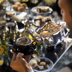 Tea being poured from a silver teapot into a black cup during a luxury dairy-free afternoon tea in Edinburgh at Prestonfield House, with elegant pastries and scones displayed in the background