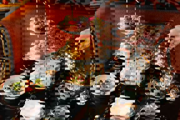 Elegant afternoon tea in Edinburgh served on a three-tier stand at Prestonfield House, featuring sandwiches, scones and pâtisserie as tea is poured at a black-lacquered table in the restaurant’s luxurious setting